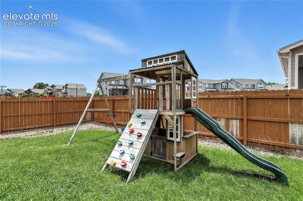 Image 36 of 42: Fenced backyard featuring a manicured lawn, a wooden play structure, and a 