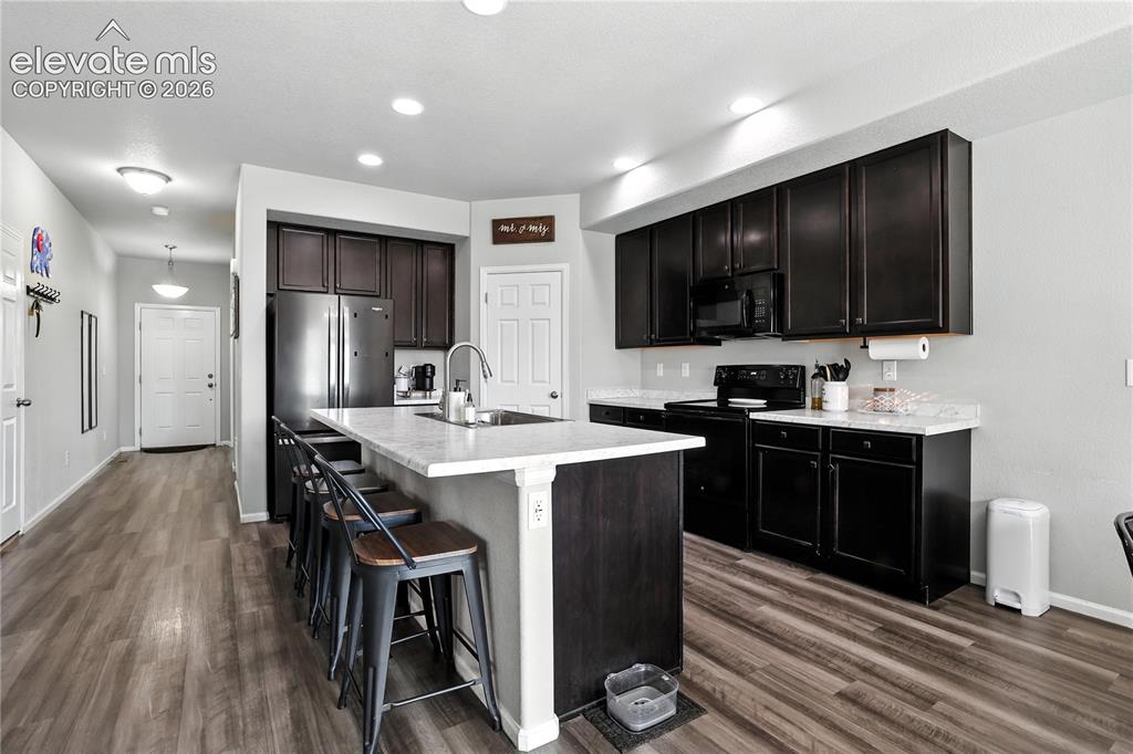 Image 4 of 42: Kitchen featuring dark wood cabinetry, light-toned countertops, and a stain