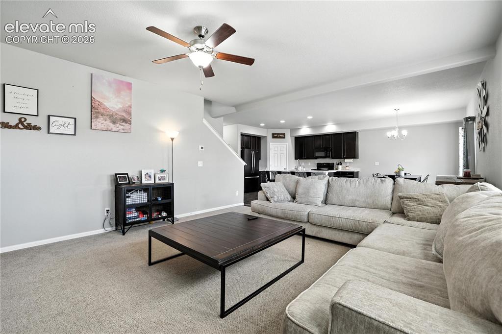 Image 9 of 42: Open-concept living space with carpeted flooring, a ceiling fan with integr
