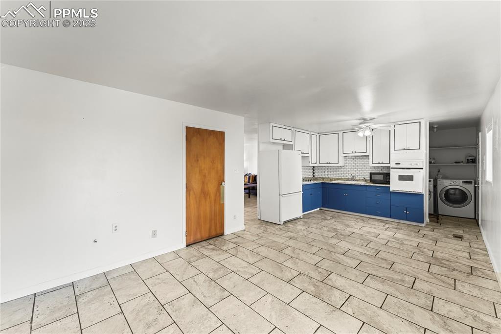 Image 18 of 27: Kitchen featuring blue cabinets, white cabinetry, white appliances, decorat