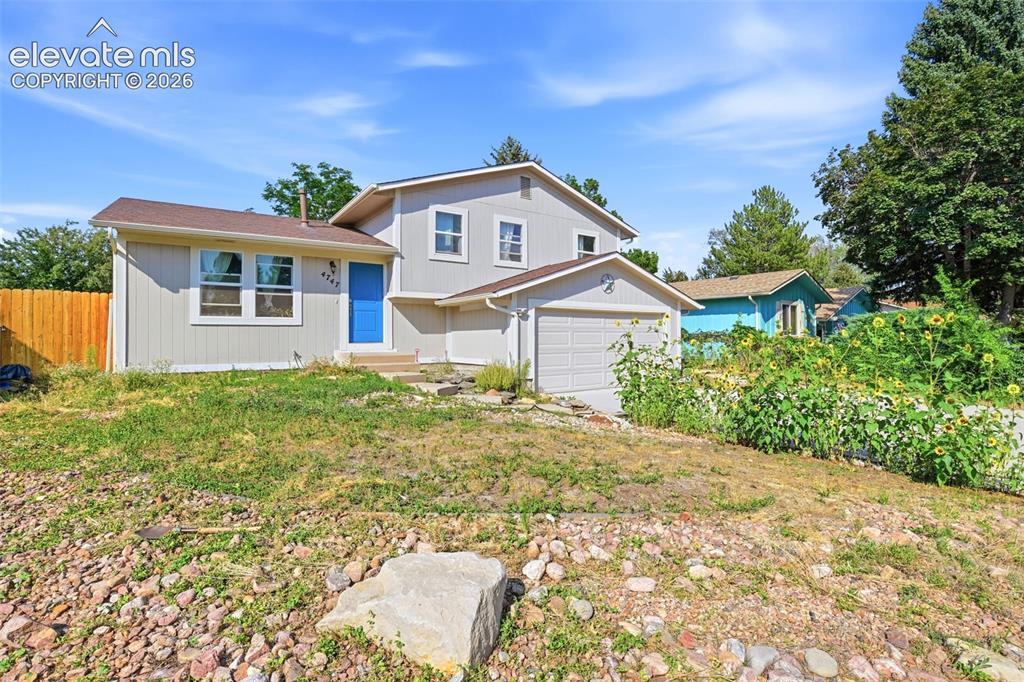 Caption: Light-toned exterior siding, bright blue entry door, attached garage, and a fenced perimeter