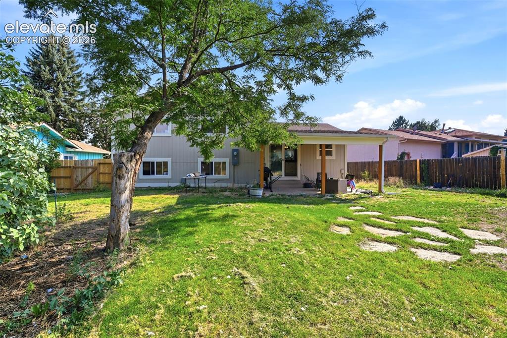Image 32 of 34: Expansive backyard featuring a covered patio, a mature shade tree, a manicu