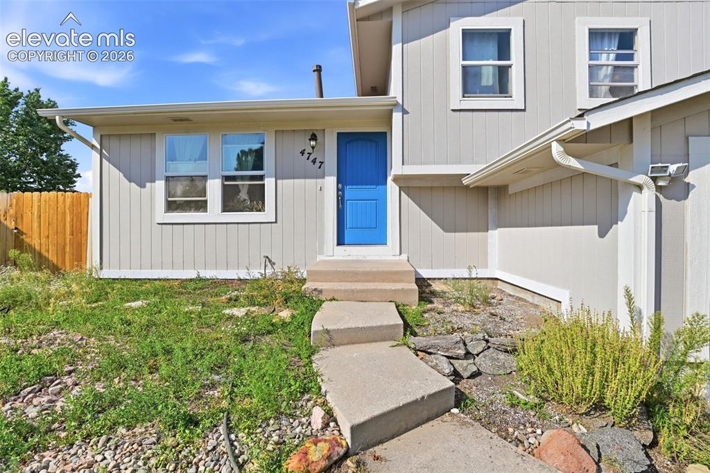 Image 4 of 34: Vertical siding exterior with a bright blue entry door, concrete pathway, a