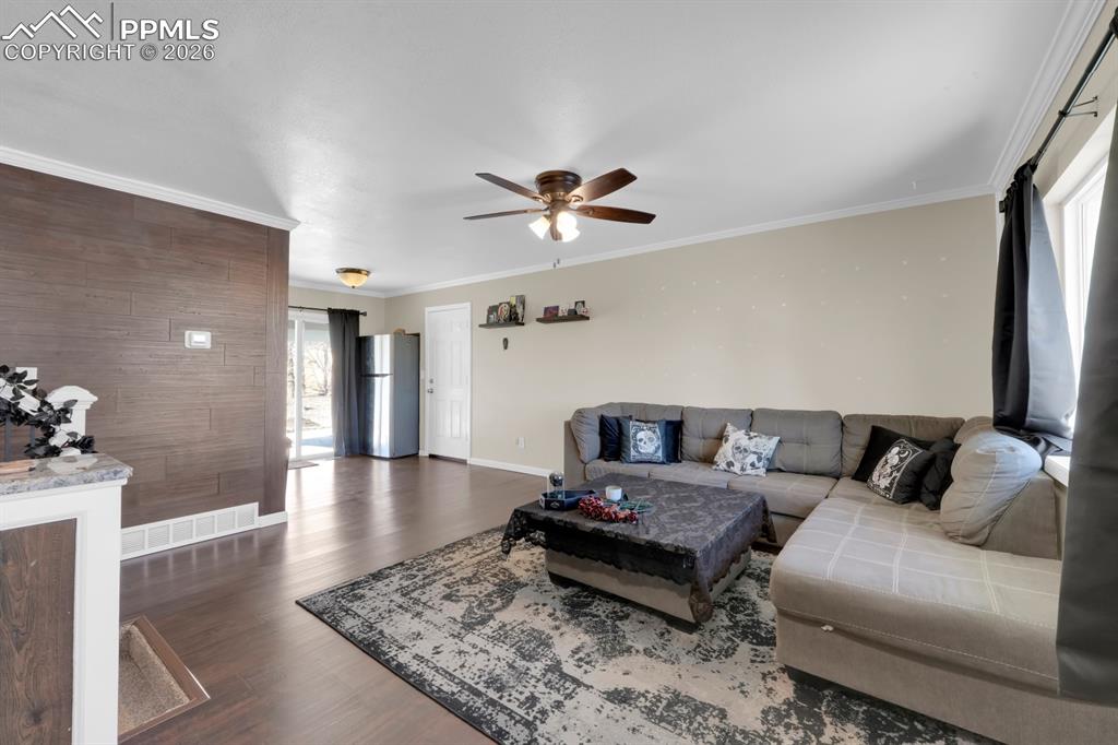 Image 2 of 29: Living room featuring a ceiling fan, crown molding, dark wood-style floorin