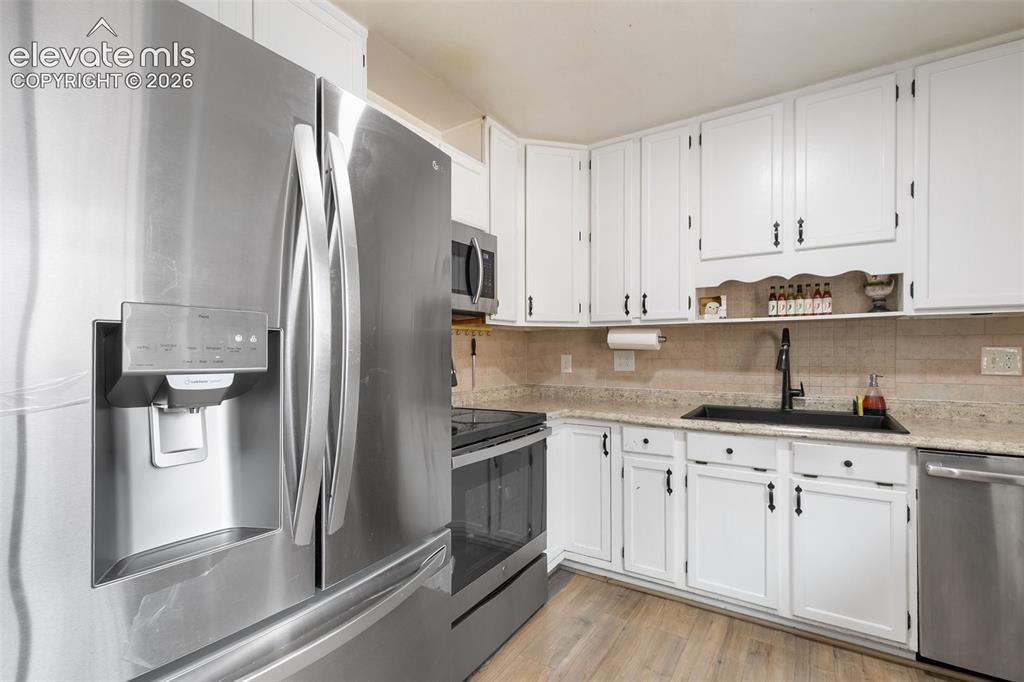 Image 11 of 29: Kitchen featuring light wood-finish flooring, white cabinetry with dark har