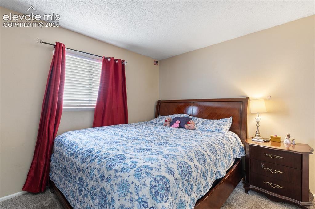 Image 12 of 29: Bedroom featuring a wood-finish bed frame with a polished headboard, neutra