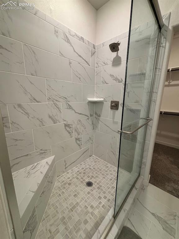 Image 32 of 49: Full bath featuring a walk in closet, a shower stall, and marble look tile 