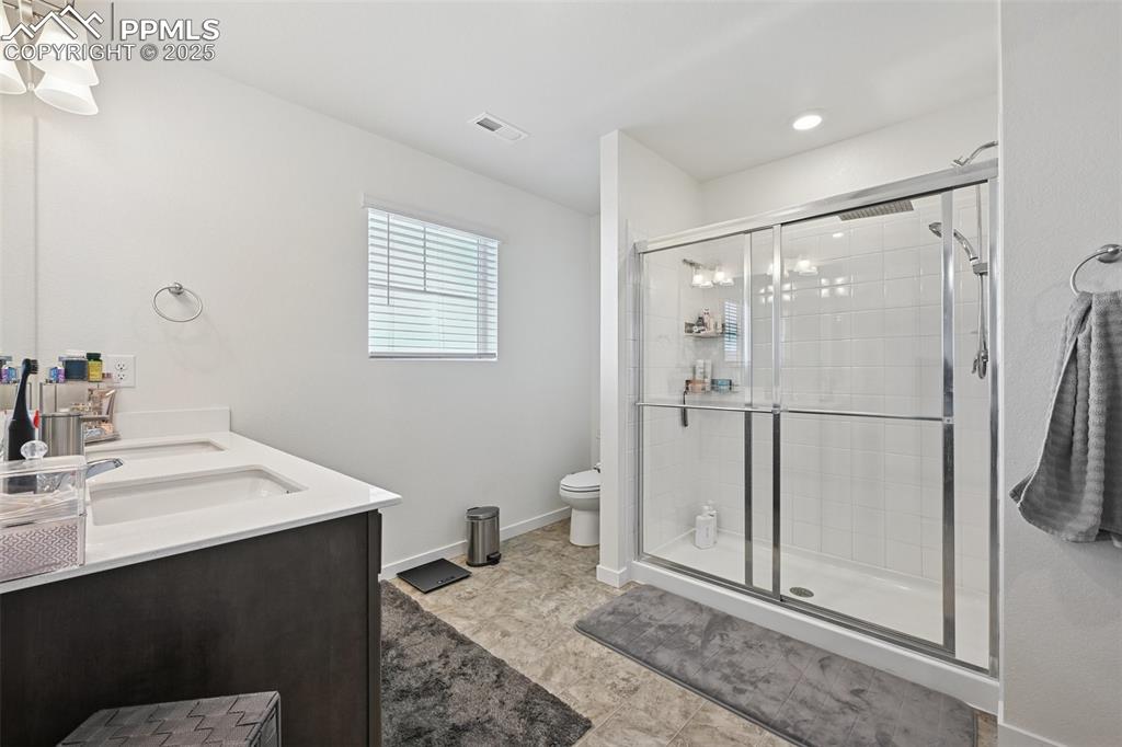 Image 27 of 35: Full bathroom featuring a shower stall, double vanity, and light tile patte