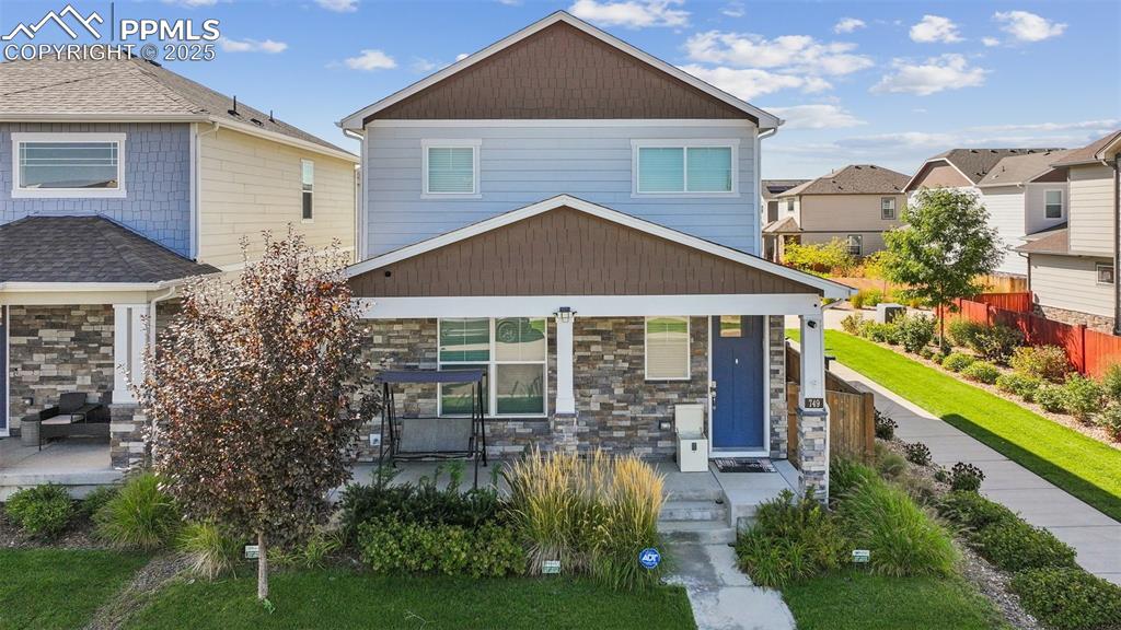 Image 4 of 35: Craftsman-style house featuring stone siding, a front yard, and covered por