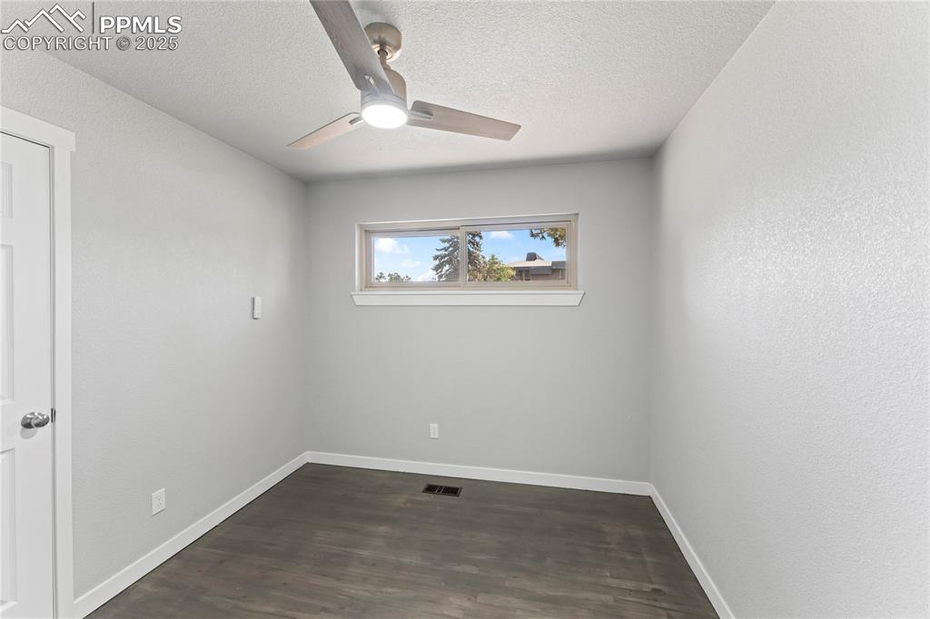Image 15 of 36: Empty room with a ceiling fan, dark wood finished floors, and a textured ce