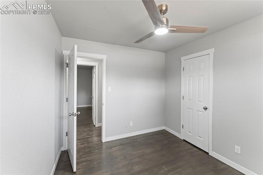 Image 16 of 36: Empty room featuring ceiling fan, dark wood-style flooring, and a textured 
