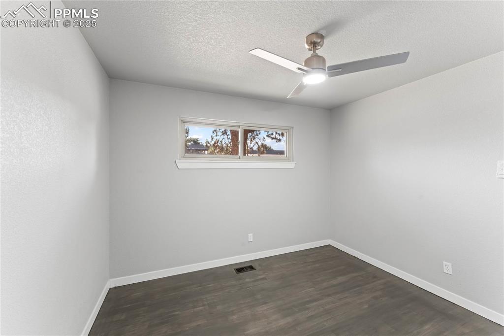 Image 19 of 36: Empty room featuring ceiling fan, dark wood finished floors, and a textured