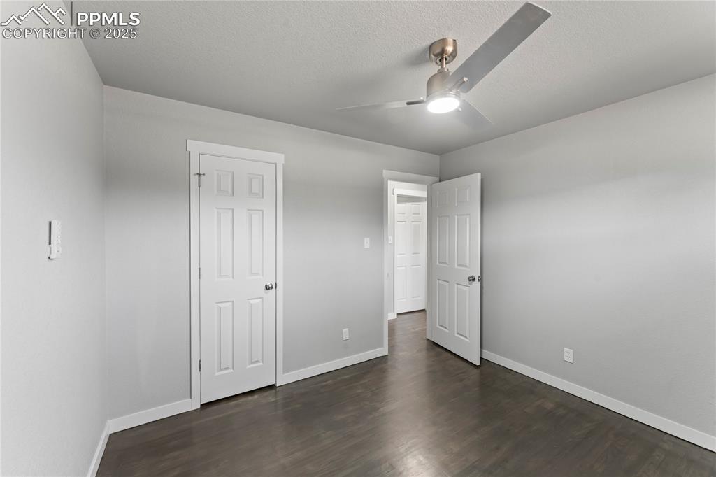 Image 20 of 36: Unfurnished bedroom featuring dark wood-style floors, ceiling fan, and a te