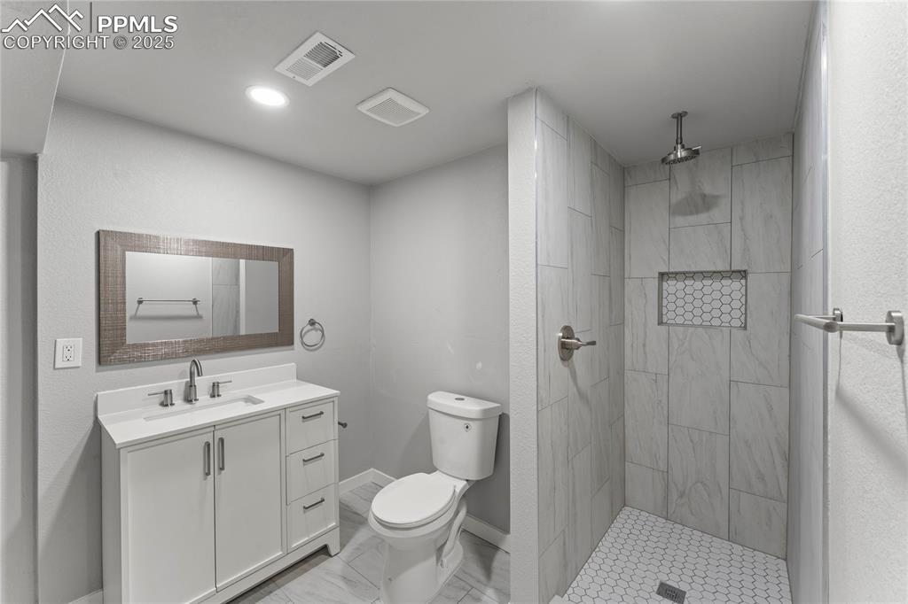 Image 28 of 36: Bathroom with vanity, a tile shower, marble finish flooring, and recessed l