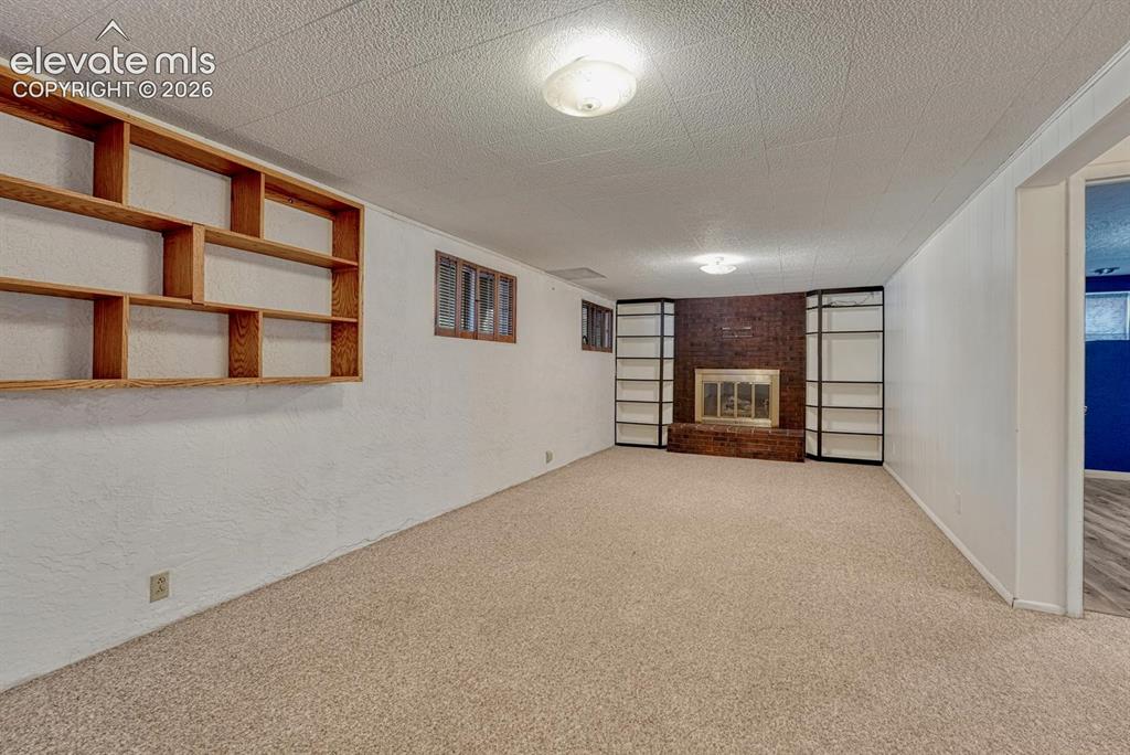 Image 35 of 50: Spacious room featuring neutral carpeting, a brick-surround fireplace with