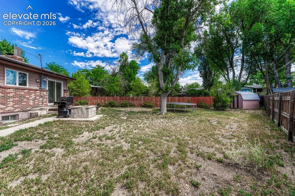 Image 43 of 50: Expansive backyard featuring a deck, built-in concrete fire pit, and mature