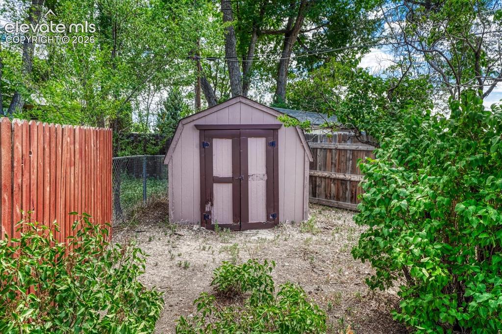 Image 44 of 50: Detached storage shed with double doors, wood siding, and an A-frame roof