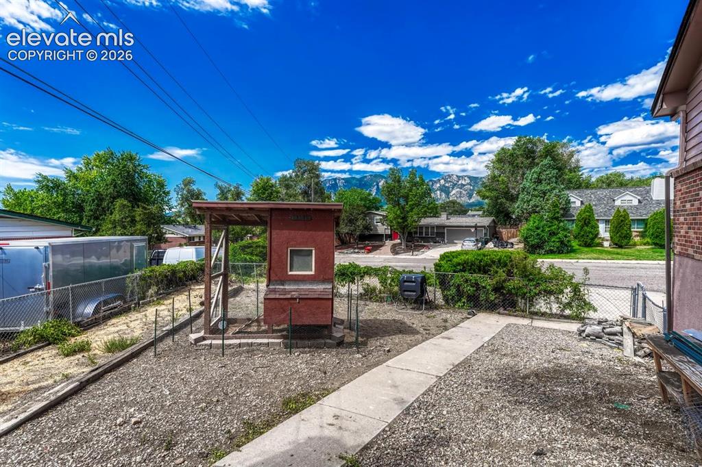 Image 45 of 50: Rear yard featuring a concrete pathway, gravel ground cover, and a chicken