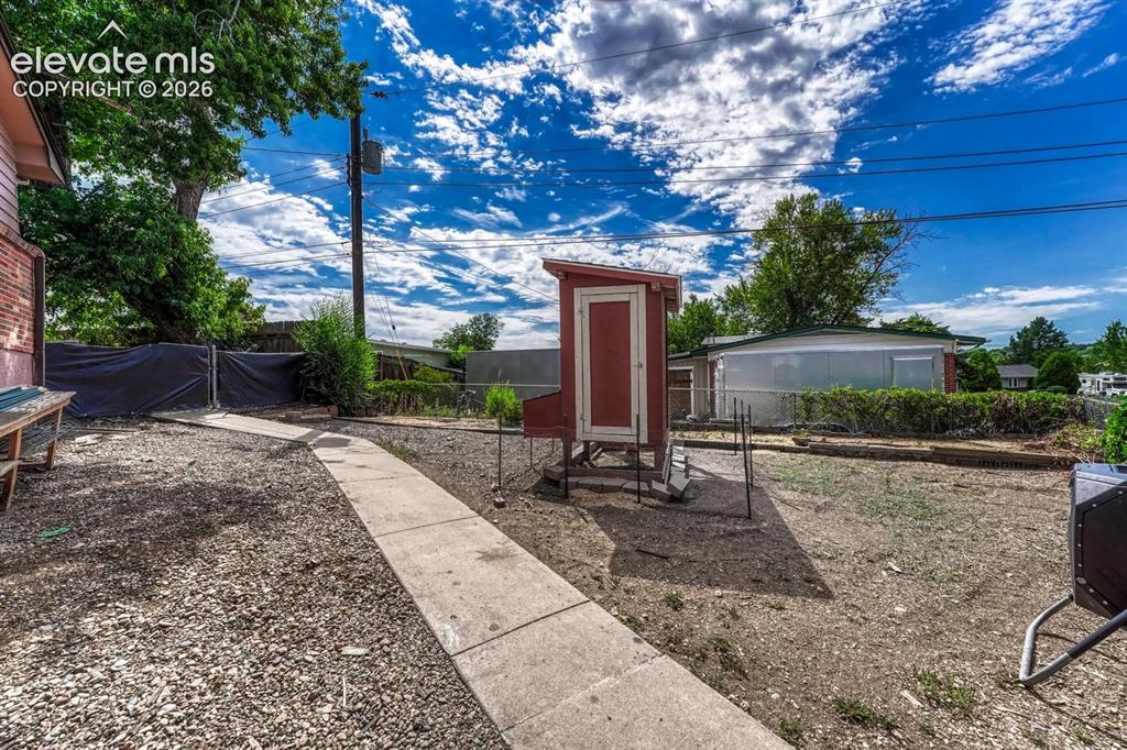 Image 46 of 50: Backyard space featuring a concrete pathway, gravel ground cover, and chick