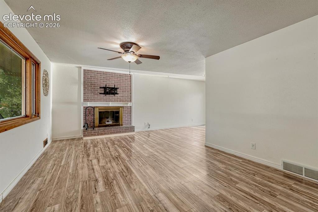 Image 5 of 50: Living area featuring laminate flooring and a brick fireplace with a brass-