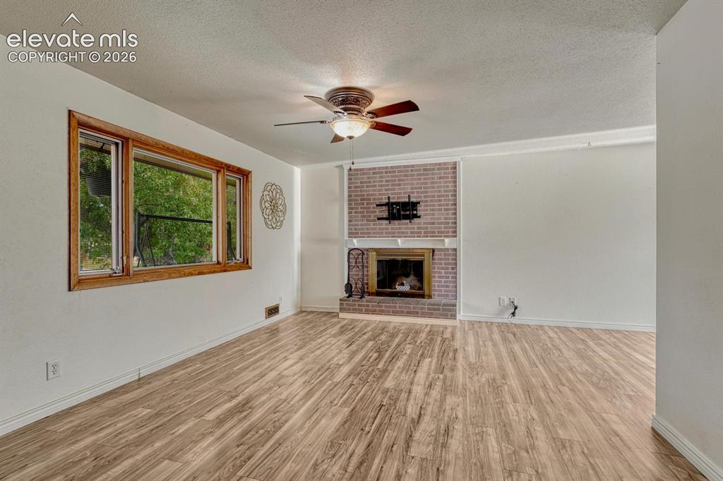 Image 6 of 50: Spacious living area featuring laminate flooring, a brick fireplace with a