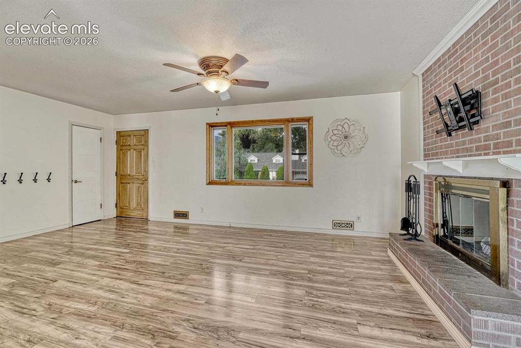 Image 7 of 50: Living area featuring a brick fireplace with a white mantel, laminate floor