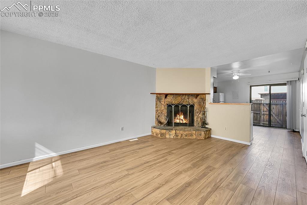 Image 4 of 12: Unfurnished living room with a fireplace, wood finished floors, a textured