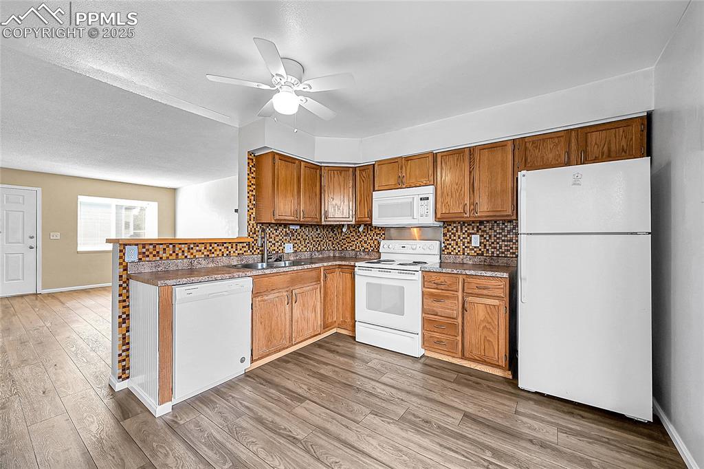 Image 6 of 12: Kitchen with backsplash, white appliances, a textured ceiling, light wood-s