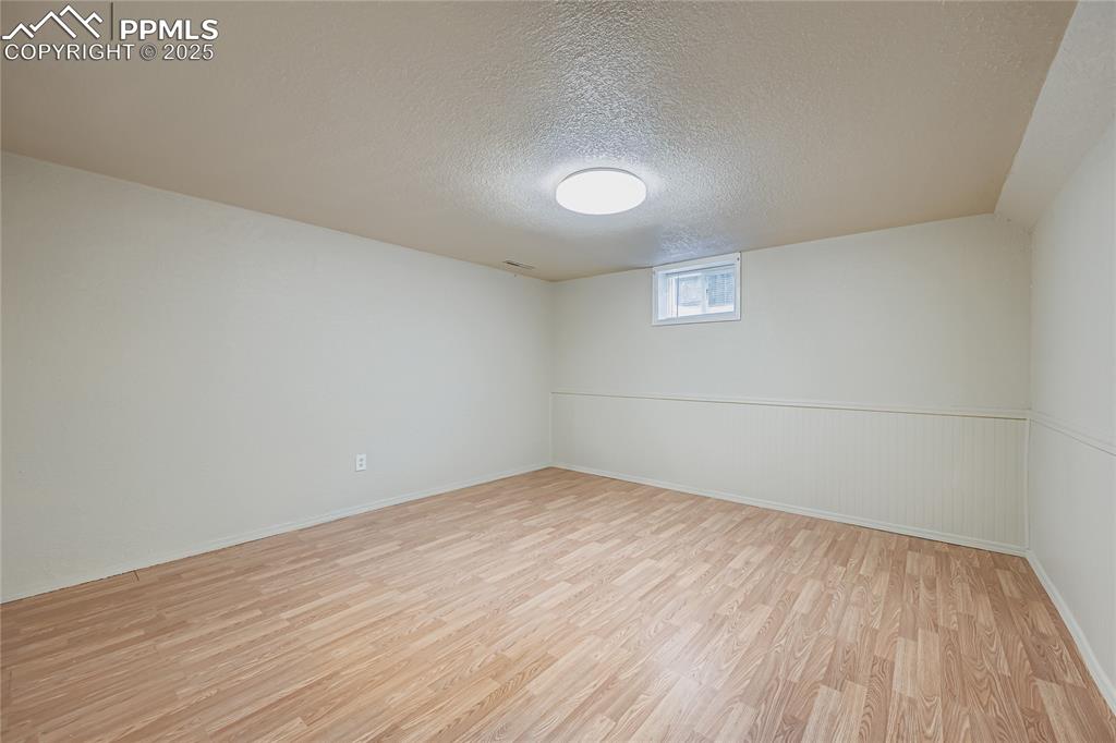 Image 19 of 25: Basement with light wood-type flooring and a textured ceiling