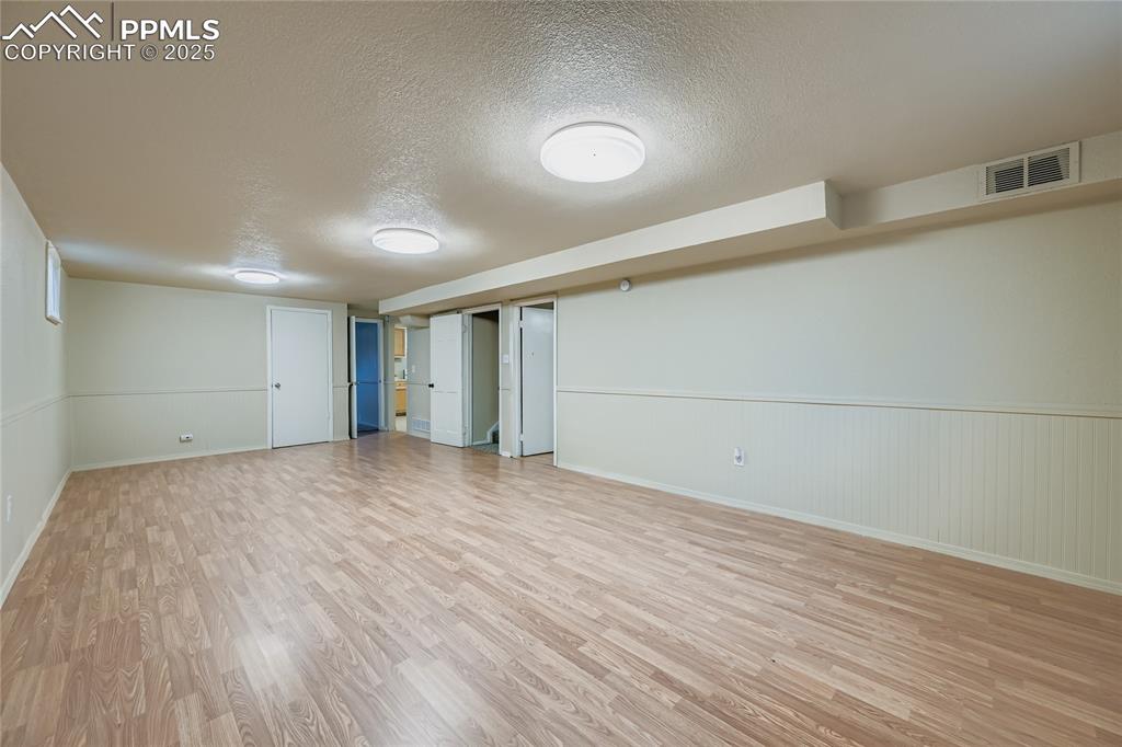 Image 21 of 25: Finished basement with a textured ceiling, a wainscoted wall, and light woo