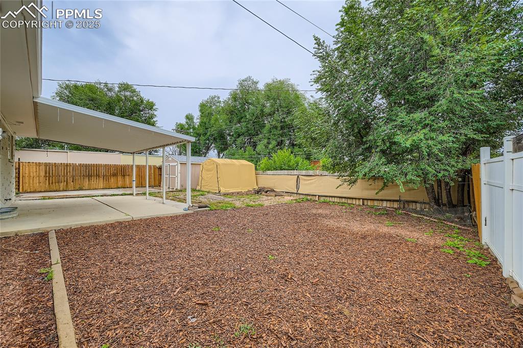 Image 22 of 25: Fenced backyard featuring a storage unit and a patio area