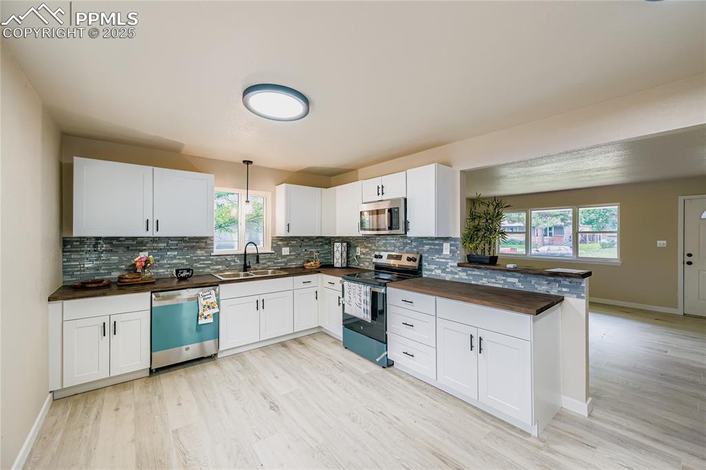 Image 3 of 25: Kitchen with stainless steel appliances, white cabinetry, pendant lighting,