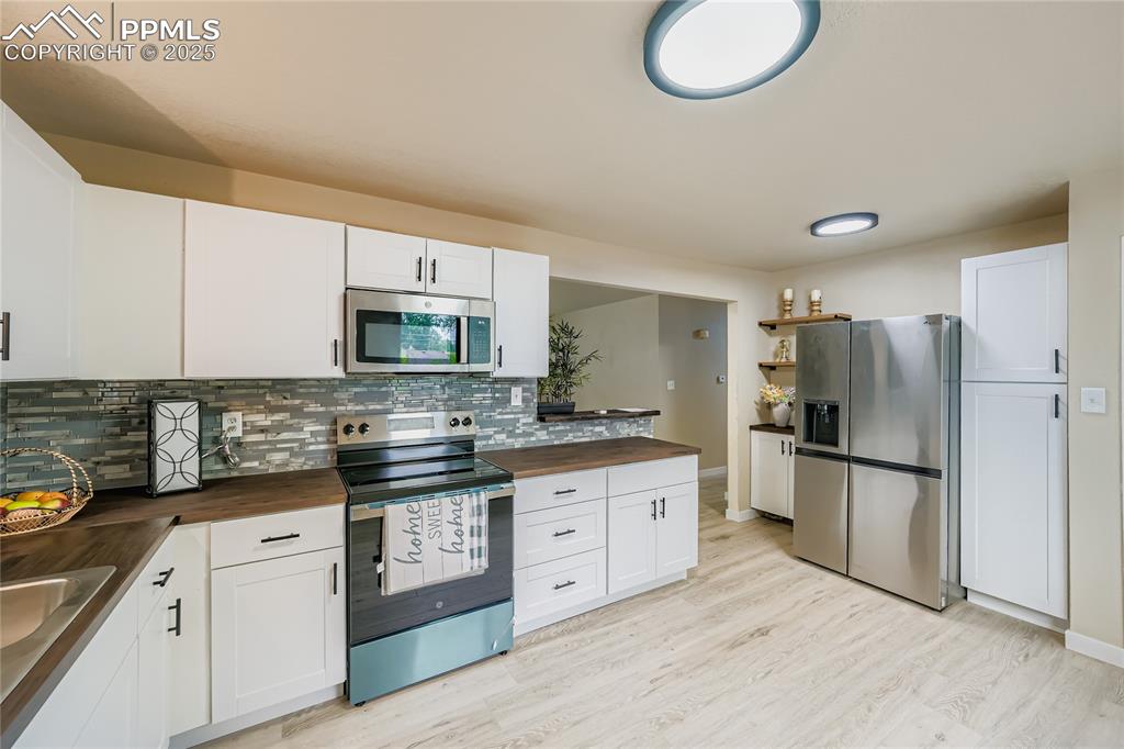 Image 4 of 25: Kitchen with stainless steel appliances, white cabinetry, and butcher block