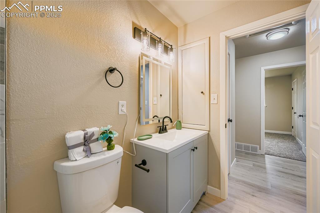 Image 7 of 25: Half bath with vanity, light wood-style floors, and a textured wall