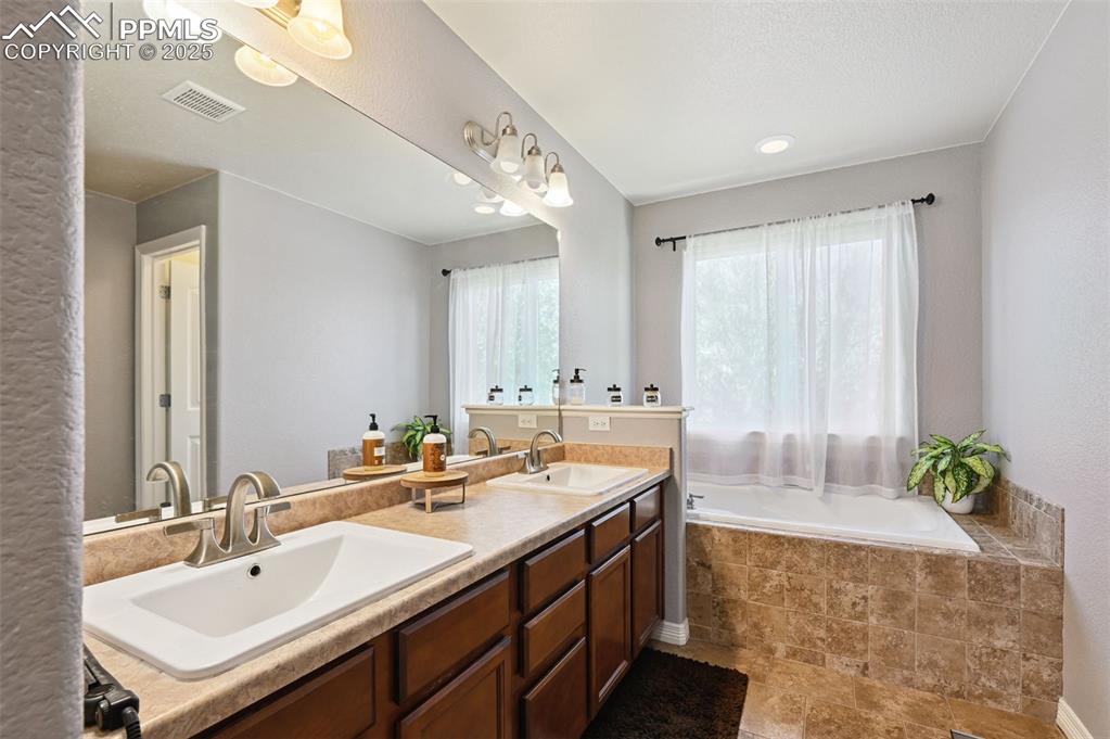 Image 14 of 39: Full bathroom with double vanity, a garden tub, and a textured wall