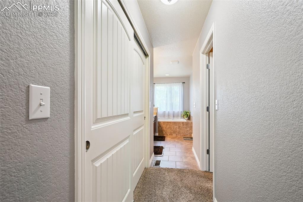 Image 31 of 39: Corridor featuring a textured wall, light colored carpet, and light tile pa