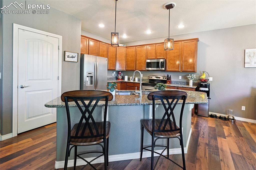 Image 5 of 39: Kitchen featuring stainless steel appliances, brown cabinets, dark wood-sty