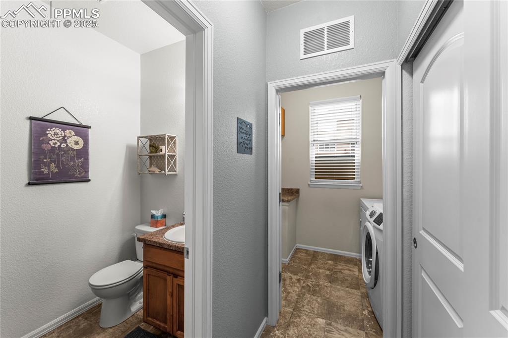 Image 14 of 39: Half bath featuring a textured wall, vanity, and aa laundry room with washe