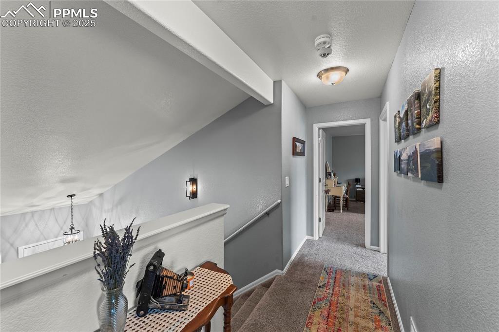 Image 24 of 39: Hall with a textured wall, a textured ceiling, carpet flooring, and an upst