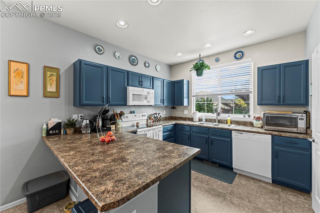Image 3 of 39: Kitchen featuring blue cabinetry, dark countertops, a textured wall, white 