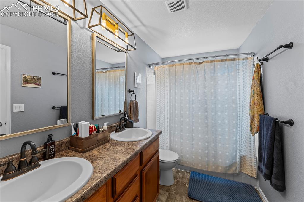 Image 33 of 39: Bathroom with a textured wall, double vanity, a textured ceiling, and showe