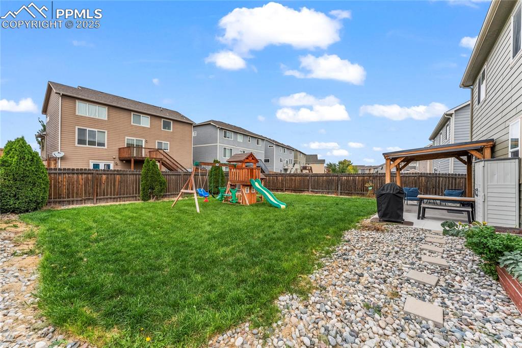 Image 36 of 39: Fenced backyard with a patio area, a playground, and a residential view