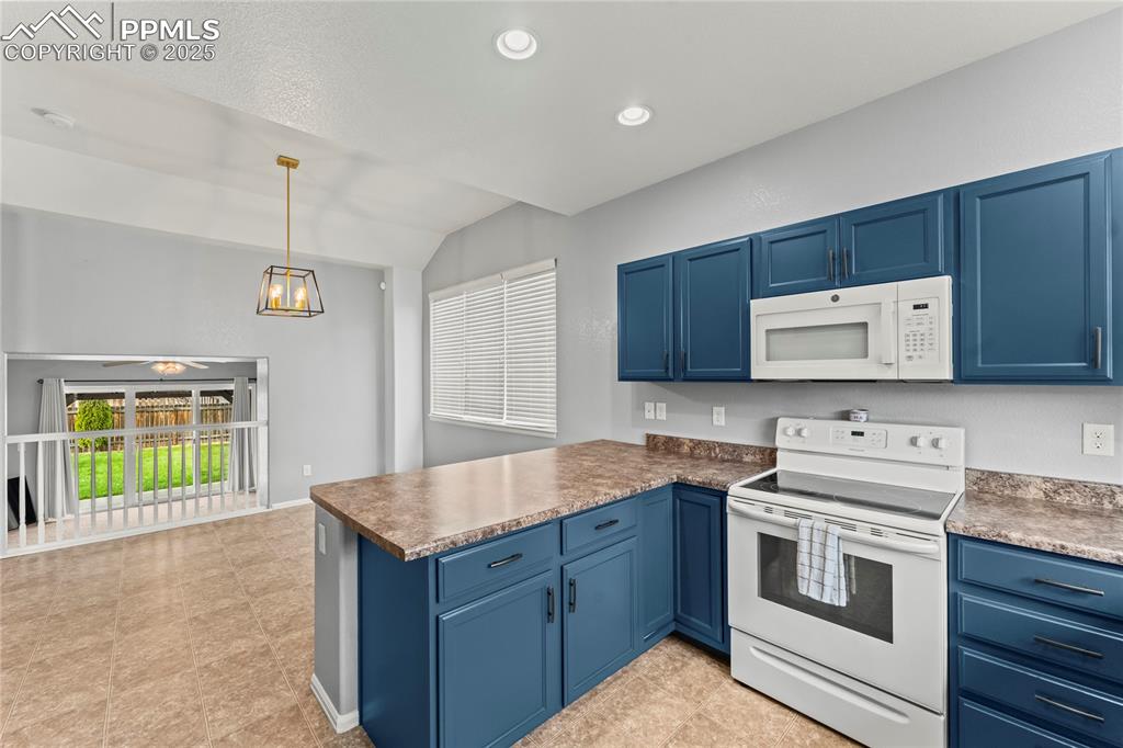 Image 7 of 39: Kitchen featuring white appliances, blue cabinets, hanging light fixtures, 