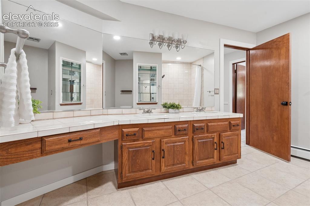 Image 37 of 50: Expansive vanity with wood-finish cabinetry, dual undermount sinks, and til