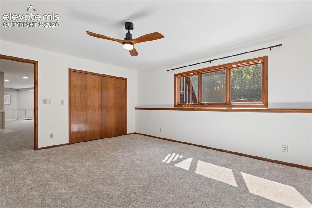 Image 39 of 50: Carpeted room with a ceiling fan, wood-framed window, and wood bifold close