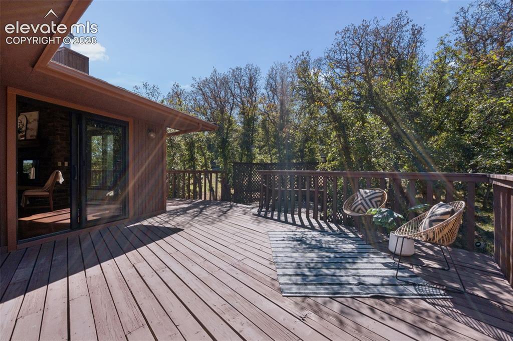 Image 46 of 50: Expansive wood-finish deck with a wood railing, surrounded by mature trees,
