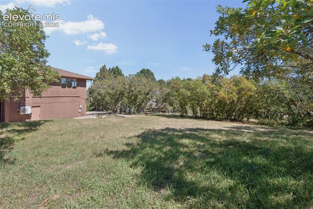 Image 47 of 50: Expansive green lawn with mature trees and a brown exterior structure
