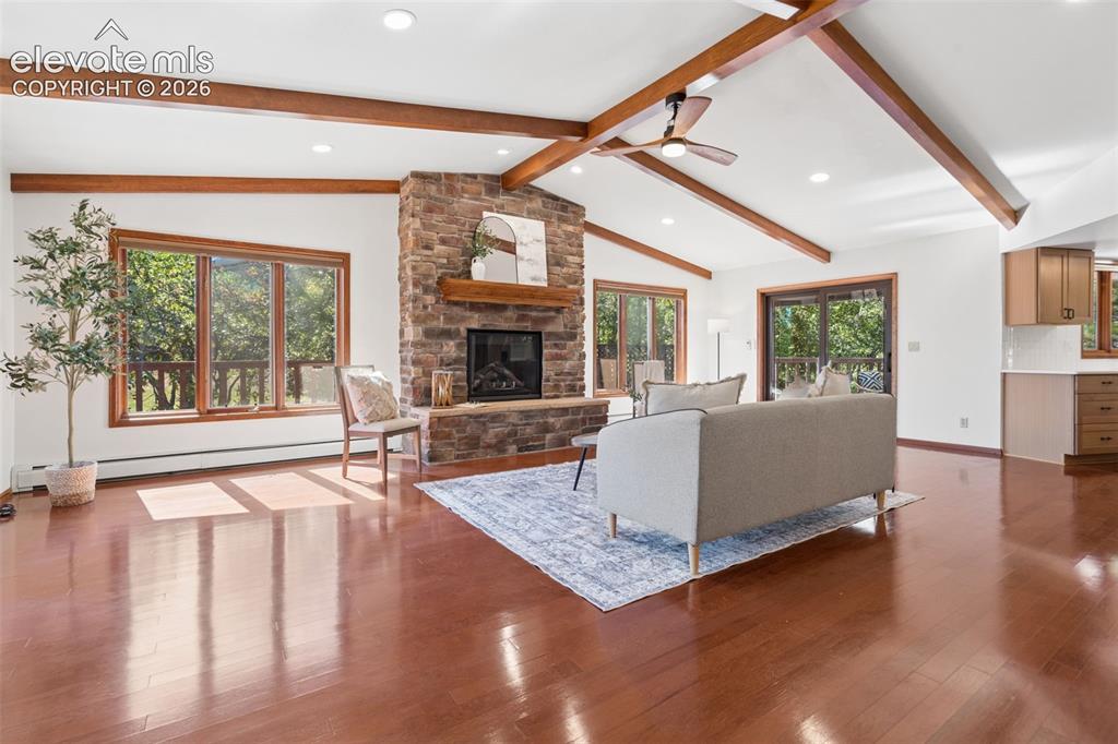 Image 6 of 50: Vaulted ceiling with exposed wood beams, stone fireplace, wood-finish floor