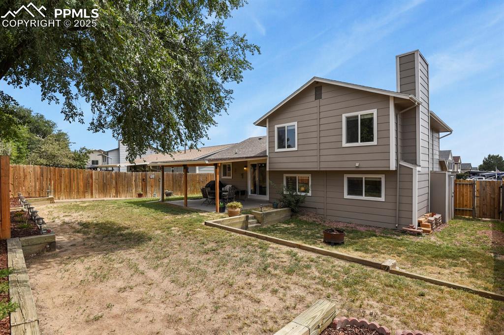 Image 26 of 31: Backyard with flower beds near fence, covered patio with new roof and garde