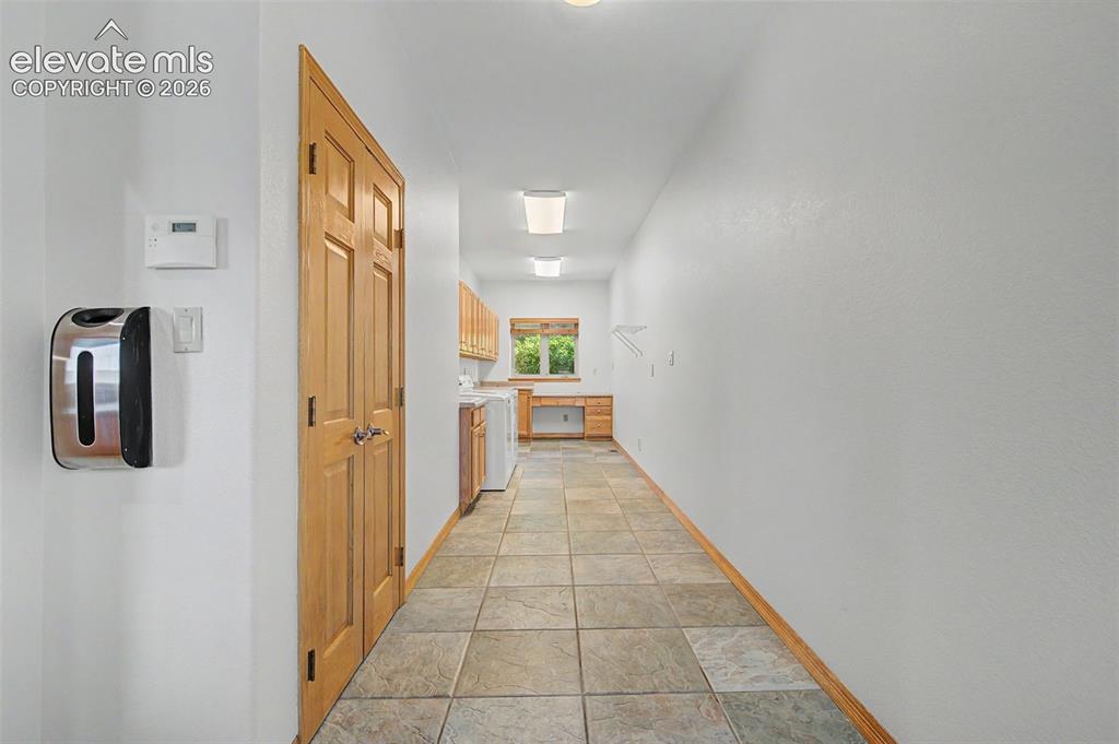 Image 31 of 50: Utility room with tiled flooring, wood-finish cabinetry, and a built-in wor